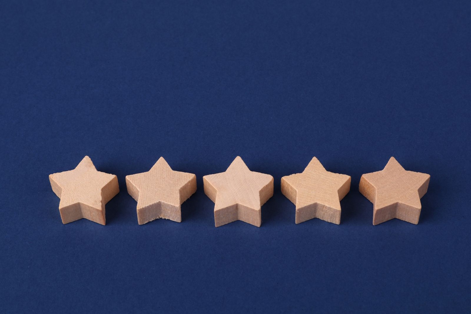 five wooden star-shaped blocks arranged in a row on a blue background, symbolizing the five-star Google reviews that build local trust signals